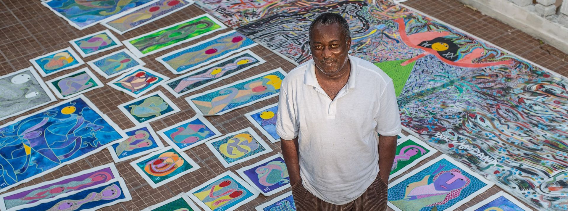 Levoy Exil standing among dozens of his colorful paintings